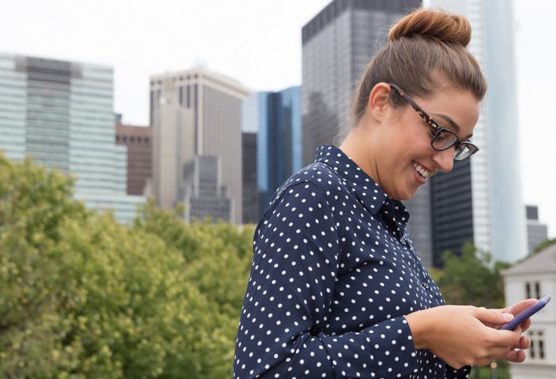 A young professional business woman texting with highrise building in the background. Photographed in New York City, in October 2015.